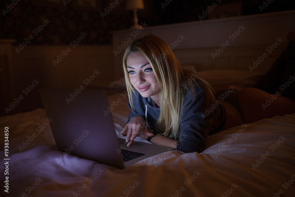 A sexy woman lying on bed with laptop at home A sexy woman lying on bed with laptop at home