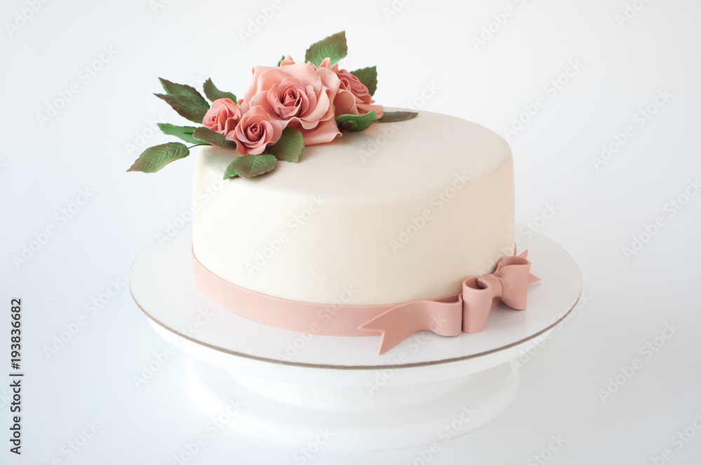 Art cake decorated with pink flowers and green leaves from mastic on a white background.