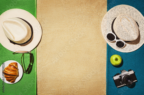 Top view of sandy beach with towel frame and summer accessories. Background with copy space and visible sand texture. Border composition made of towel