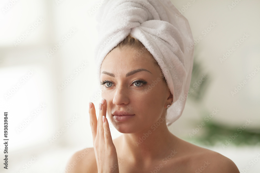 Young woman with flawless skin, applying moisturizing cream on her face. Photo of woman after bath in white bathrobe and towel. Skin care concept Young woman with flawless skin, applying moisturizing cream on her face. Photo of woman after bath in white bathrobe and towel. Skin care concept