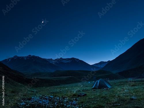 Late evening at Caucasus mountains. Camping at Kvakhidi meadows in Tusheti (Georgia). Green tent stands at the meadow. Nautical blue skies above it. Mountain range on the background.