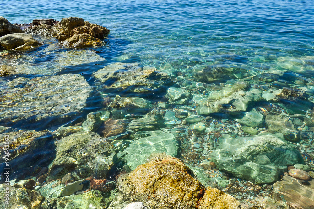 Transparent sea water seethes at the shore. Large coastal colored stones in the water. Beautiful abstract background.