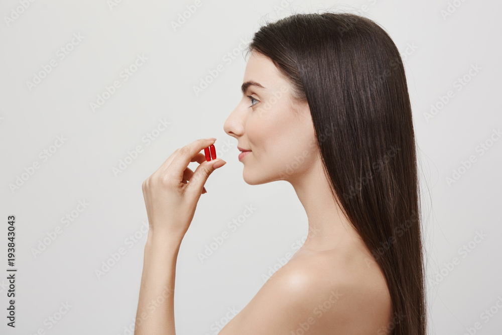Profile portrait of attractive healthy european woman taking medicine or vitamins, holding two pills near mouth and being in great mood, wanting to make her body irresistible to illnesses Profile portrait of attractive healthy european woman taking medicine or vitamins, holding two pills near mouth and being in great mood, wanting to make her body irresistible to illnesses