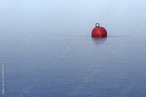 red buoy frozen in ice on the blue water in a lake or the sea, abstract background for winter season and yachting break, metaphor of deadlock, generous copy space