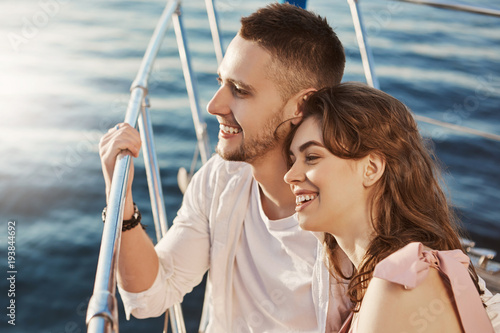 Two beautiful married people in love, smiling broadly while sitting at bow of boat and holding handrail. Couple of young adults in relationship share stories about their exes.