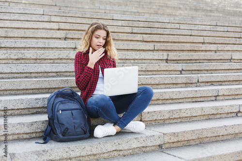 Female student sitting on the stairs and working with laptop outdoors © Prostock-studio