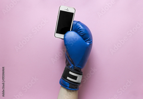 on a pink background a hand in a boxing glove of blue color with a phone in hands  photo