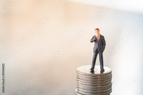 Money and Business Concept. Businessman miniature figure standing on stack of silver coins.