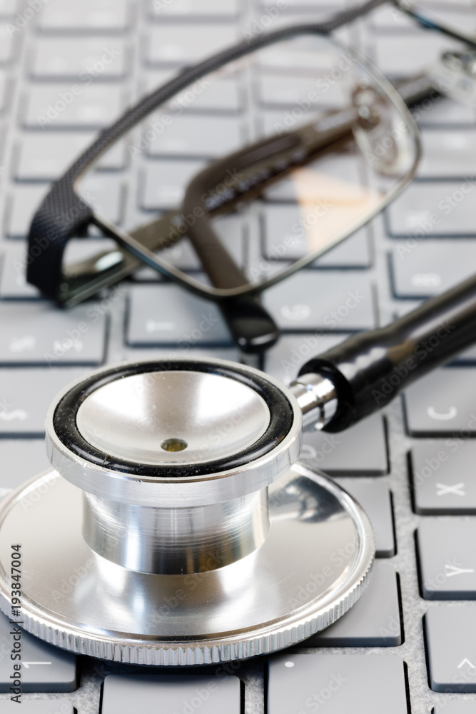 Brille und Stethoskop auf einer Computertastatur Brille und Stethoskop auf einer Computertastatur