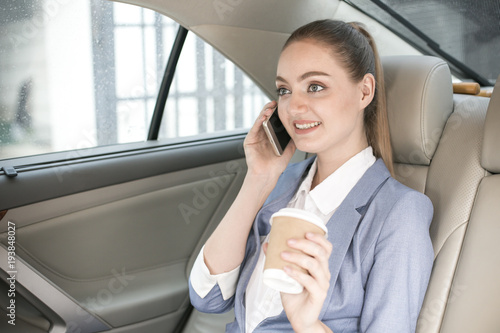 Attractive female using a smartphone while sitting in a car to go to work, Woman working overtime concept.