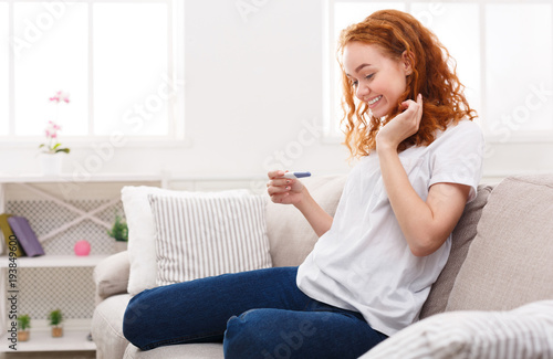 Happy girl with pregnancy test sitting on sofa