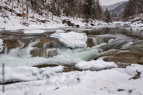 Winter landscape. Mountain river flows from the rocks. Snow and mountain river