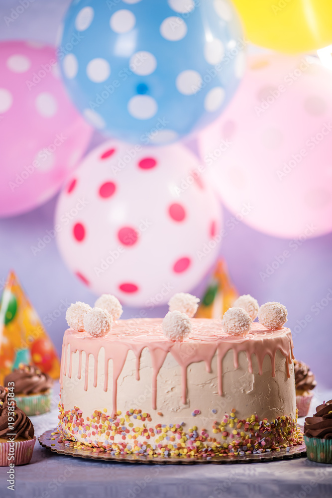 detail of a pink white birthday cake with coconut balls colorful balloon background detail of a pink white birthday cake with coconut balls colorful balloon background