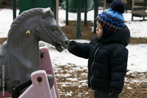 Two year toddler playing with a toy horse. Kid feeding wooden horse