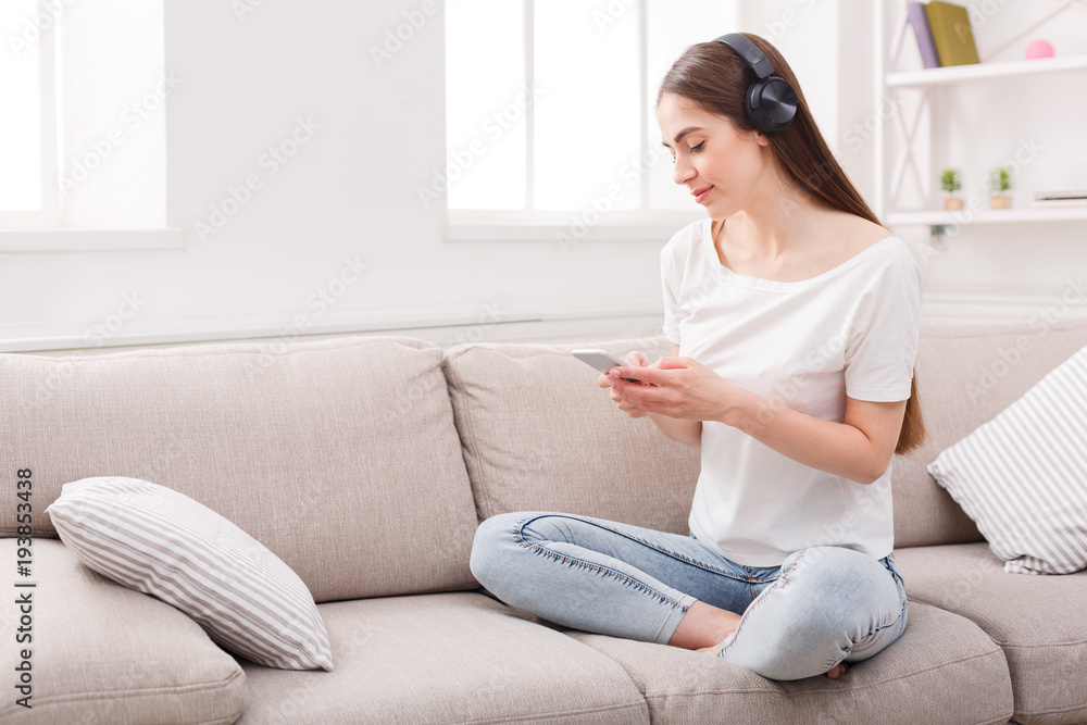 Young woman with cell phone and headphones on beige couch
