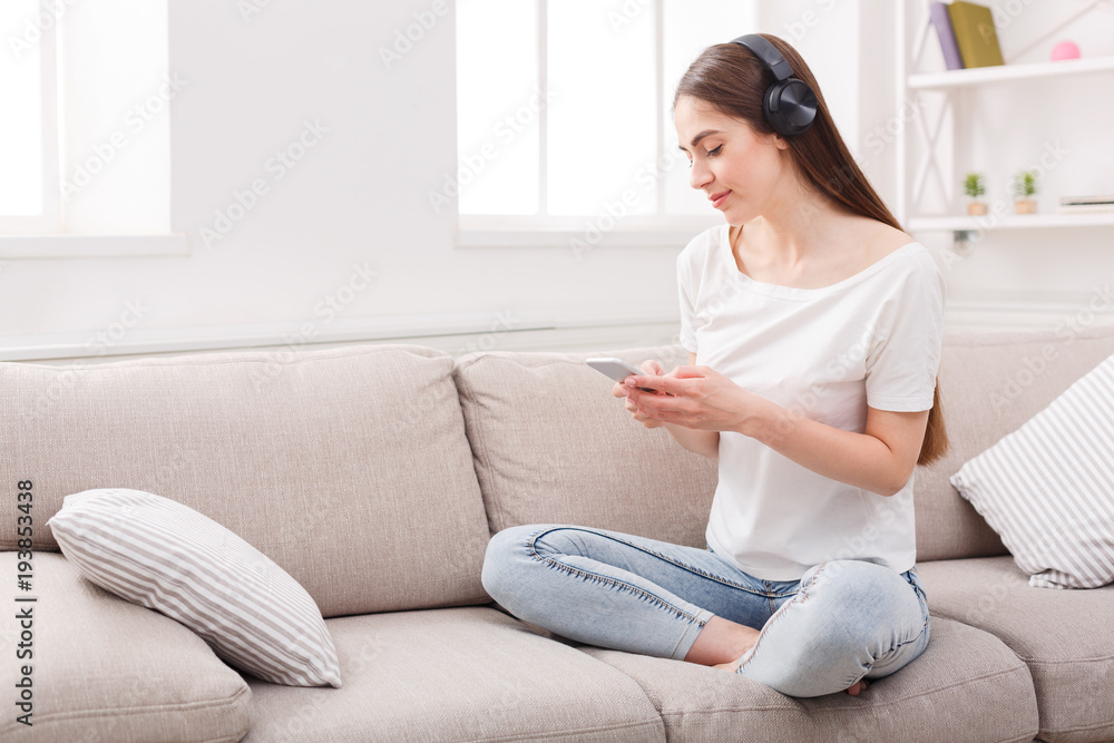 Young woman with cell phone and headphones on beige couch Young woman with cell phone and headphones on beige couch