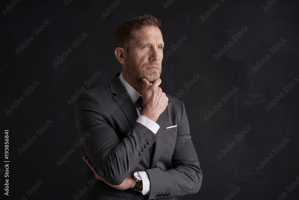 Nervous, overwhelmed businessman portrait.  Stressed businessman hand is on his forehead while sitting at dark background and thinking very hard. Professional man wearing suit.