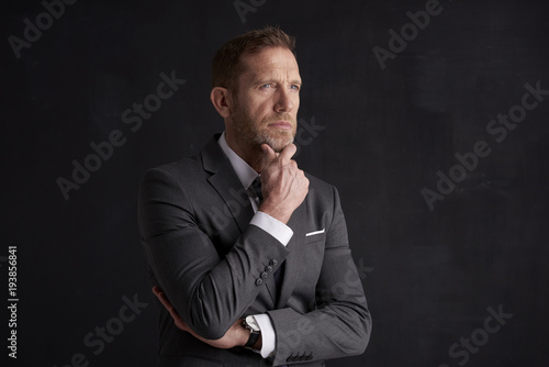 Nervous, overwhelmed businessman portrait. Stressed businessman hand is on his forehead while sitting at dark background and thinking very hard. Professional man wearing suit.