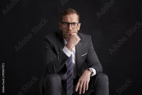 Thinking businessman portrait. Studio shot of wrinkled face business man wearing suit and looking thoughtful while sitting at dark background. Professional man wearing suit and tie. 