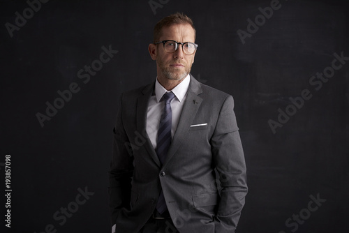 Executive senior businessman portrait. Middle aged financial director business man wearing suit and looking at camera while standing at dark background. 