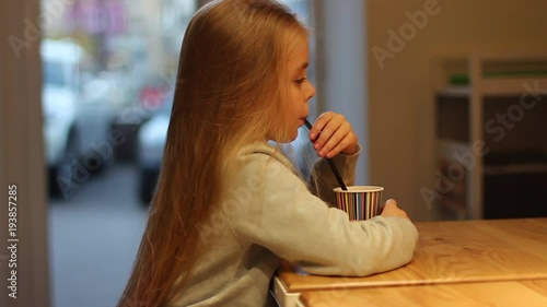 Beautiful, little, pretty girl with long hair sitting in cafe, drinking cocoa