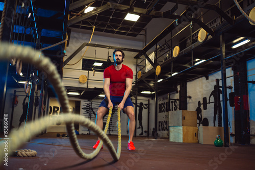 Attractive muscular man working out with heavy ropes. Crossfit.