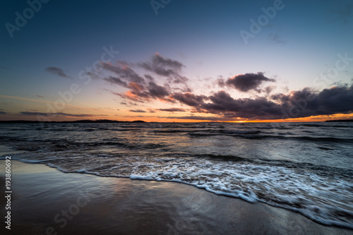 waves rushing onto a sandy beach at sunset