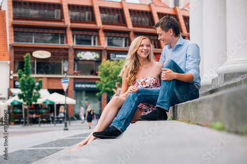 Young happy couple hugging on the street sitting on the stairs. Smiling man and woman having fun in the city.