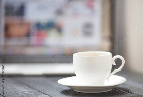 Coffee Cup on the white table on blurred laptop background for Business Concept.