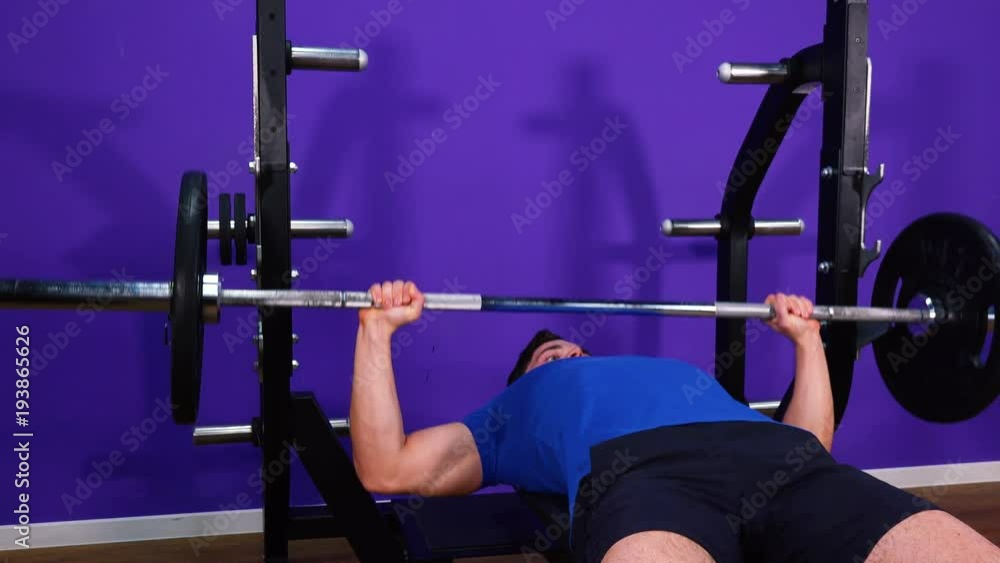 A young fit man does bench press in a gym - closeup A young fit man does bench press in a gym - closeup