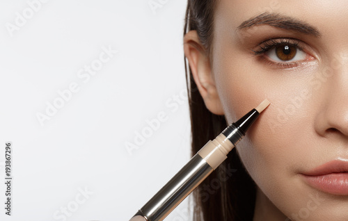 Close up of half female face. Confident young woman is applying concealer on her cheek. Isolated and copy space