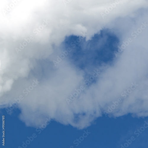 A hole in the form of a heart in a white cloud against a blue sky. A square picture. Background for design. Copy space. © romsvetnik