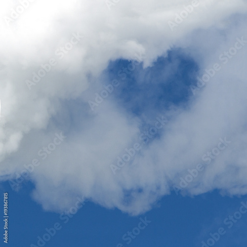 A hole in the form of a heart in a white cloud against a blue sky. A square picture. Background for design. Copy space.