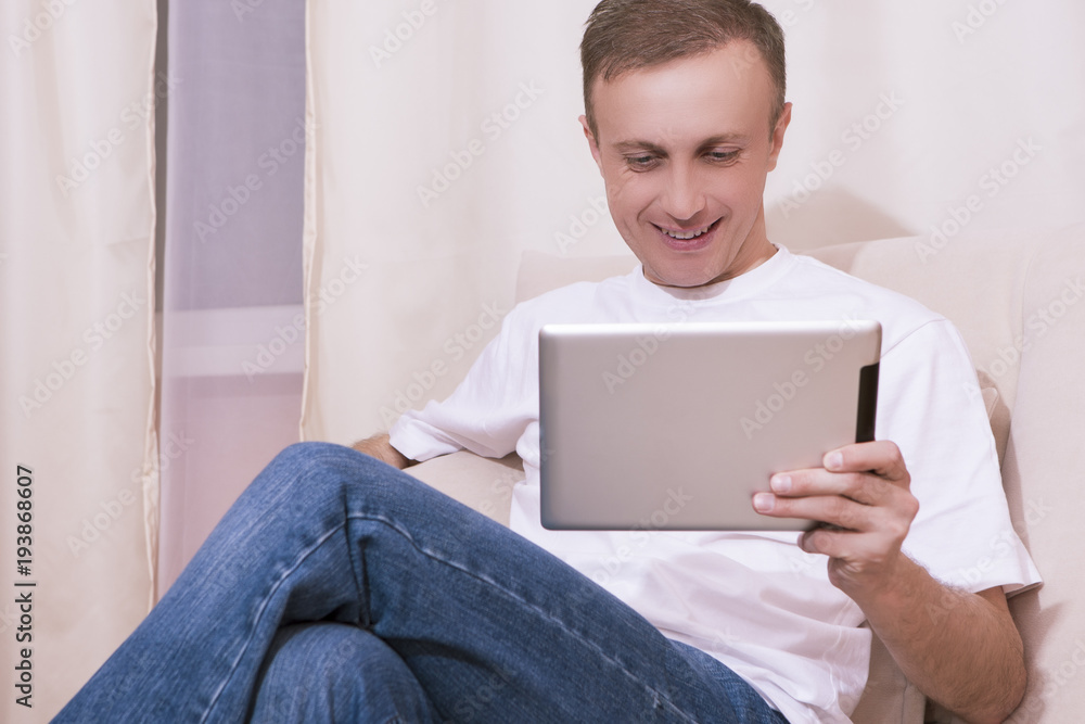Youth Lifestyle Ideas and Concepts.Happy Caucasian Man with Tablet Computer on Couch. Posing Indoors in Home Environment. Youth Lifestyle Ideas and Concepts.Happy Caucasian Man with Tablet Computer on Couch. Posing Indoors in Home Environment.