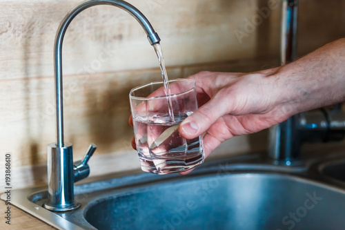 hand holding a glass of water. a man  pouring water from filter tap. clean water and healthy life concept