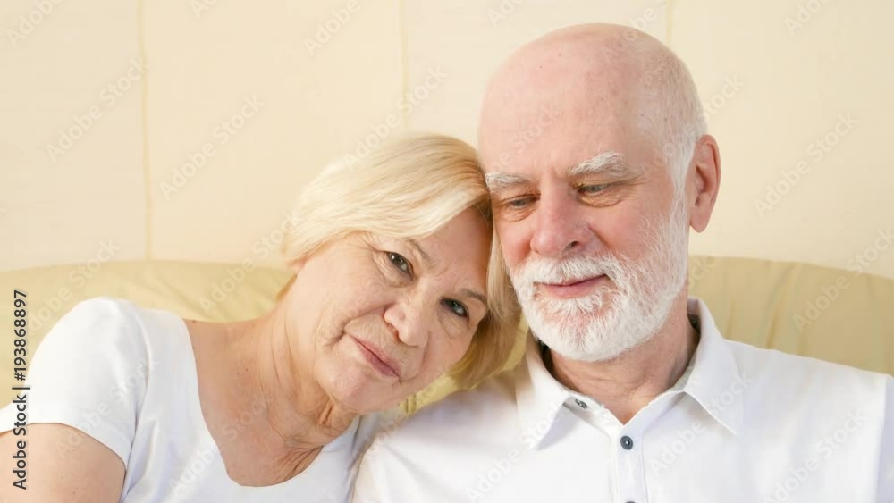 Portrait of cheerful good-looking senior couple sitting on couch at home. Having good time relaxing together. Portrait of cheerful good-looking senior couple sitting on couch at home. Having good time relaxing together.