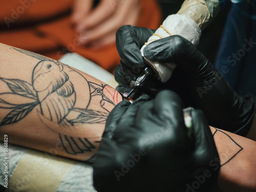 Tattoo artist at work. Woman in black latex glove tattooing a young man's hand with colorful picture in studio. Macro. © kohanova1991
