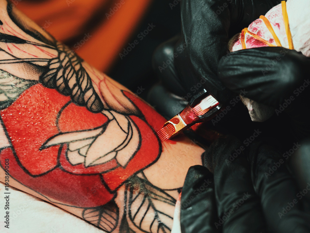Tattoo artist at work. Woman in black latex glove tattooing a young man