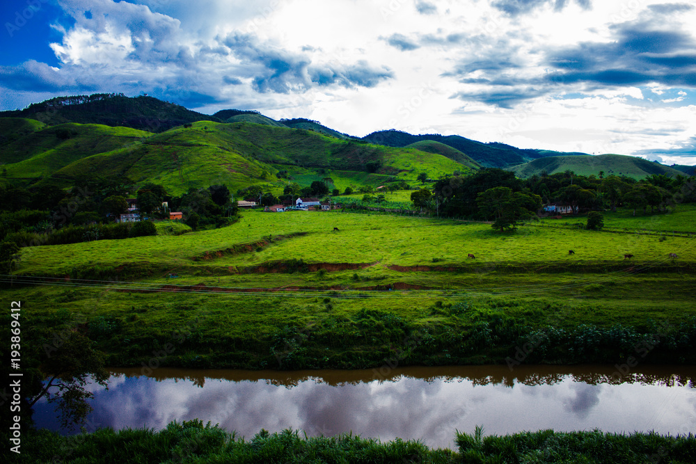 Green mountains, a cloudy blue sky and a river. 