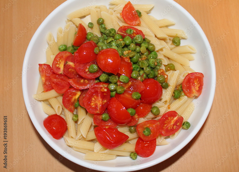 Penne pasta with cherry tomatoes and peas in a white bowl.
