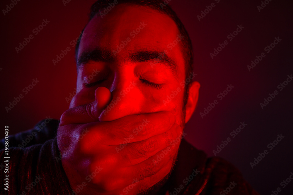 Closeup of a mans hand covering a man mouth with terrified facial expression Closeup of a mans hand covering a man mouth with terrified facial expression