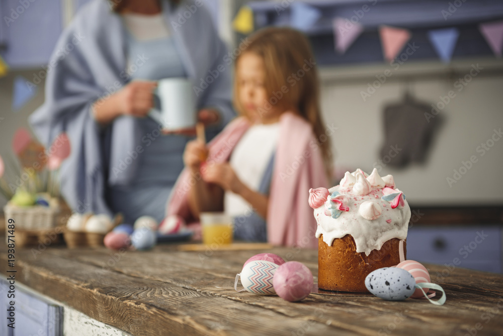 Fototapeta premium Serene mother and child colorizing eggs. Focus on traditional sweet bread standing on table