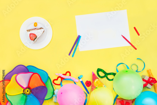 Bright yellow background with festive cake, empty blank, party tools and decoration - baloons, funny carnival masks, festive tinsel, garland with flags. Happy birthday design concept. Place for text.