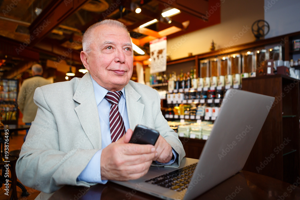 Old senior businessman in suit and tie with laptop computer and smartphone, sitting in city cafe house Old senior businessman in suit and tie with laptop computer and smartphone, sitting in city cafe house
