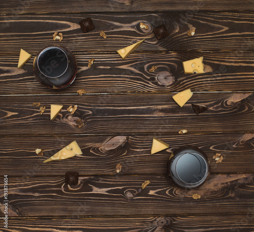Two glasses of wine, cheese, Greek walnut, chocolate candies on a wooden background, top view