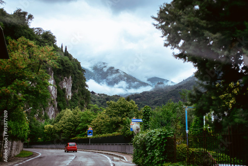 Italy Lake Como Wideangle lens shot of red italian car at mountain road with tunnel among forest at foggy rainy day of June photo