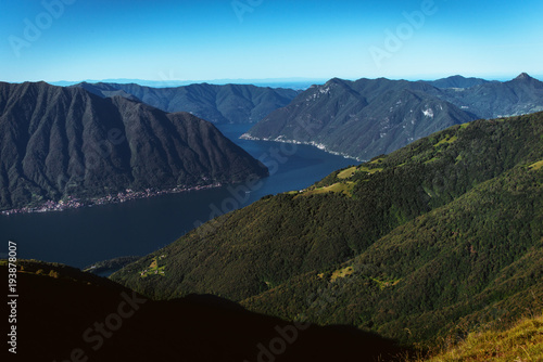 Panoramic View of beautiful landscape in the Italian Alps with fresh green meadows and snow-capped mountain tops in the background on a sunny day with blue sky and clouds in springtime.