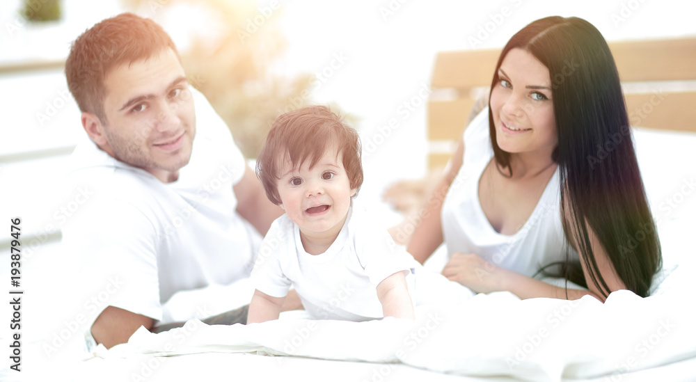 Happy young family with a baby lying in bed and smiling Happy young family with a baby lying in bed and smiling