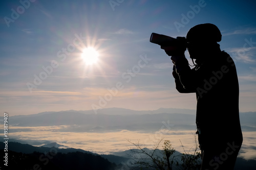 Silhouette of free and happy photographer with camera at sunset time on the mountain view. Freedom, success and triumph concept