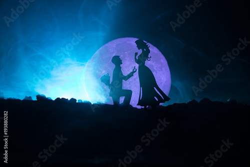 Amazing love scene. Silhouettes of man making proposal to woman or Silhouettes of couple against big moon at background